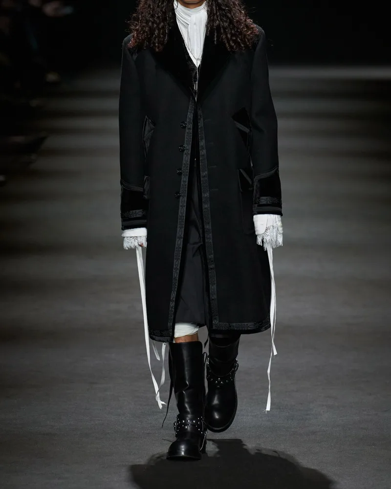 Модель Ann Demeulemeester в длинном черном пальто и черных сапогах с пряжкой и заклепками