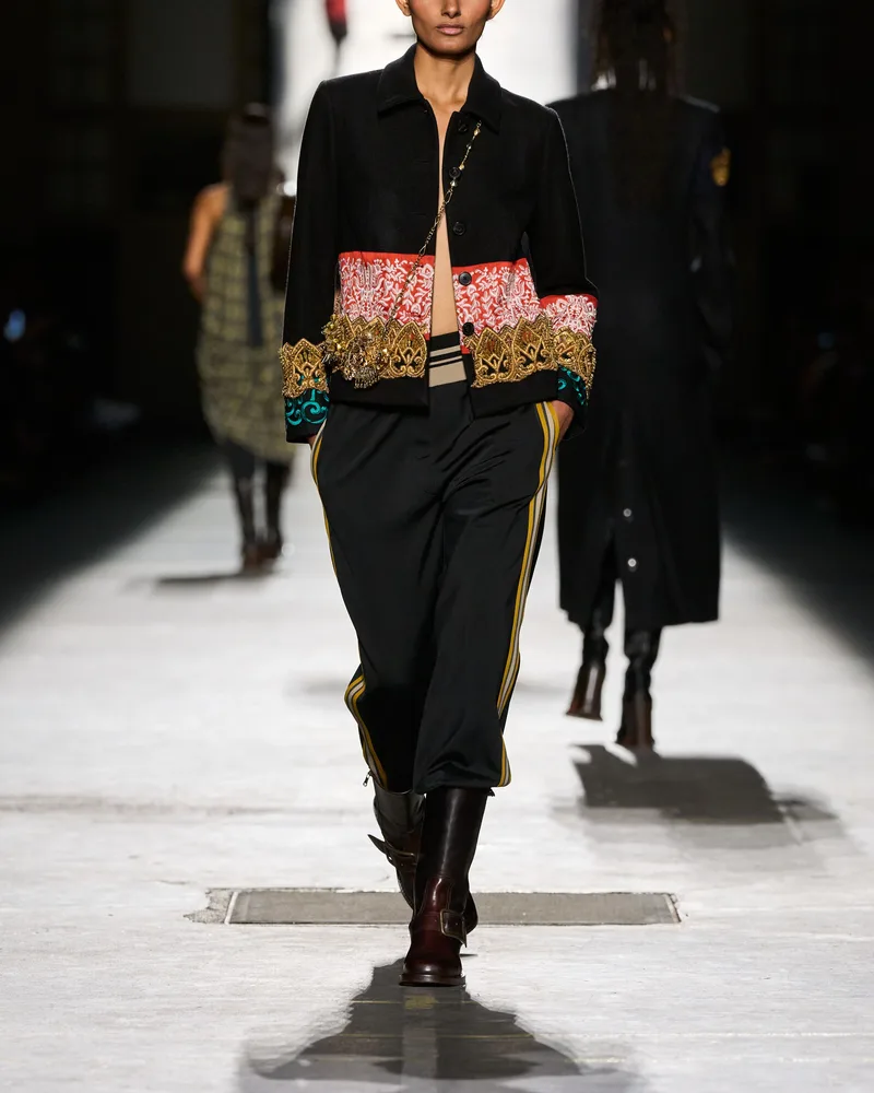Модель Dries Van Noten в черных брюках с лампасами, заправленных в сапоги с пряжкой, и короткой куртке