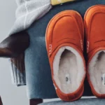 Оранжевые замшевые лоферы UGG x JW Anderson с белой овчиной внутри на синем бархатном кресле
